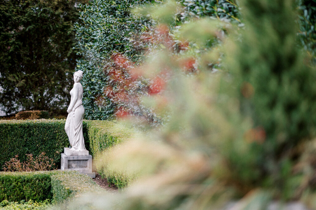 Marble statue of a woman stands beside a hedge in the manicured gardens of the Park Chateau wedding venue