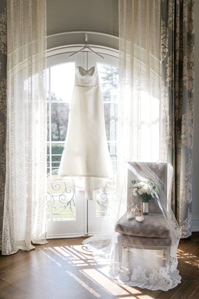 White wedding dress hangs in front of arched french doors that overlook the gardens at the Park Chateau wedding venue