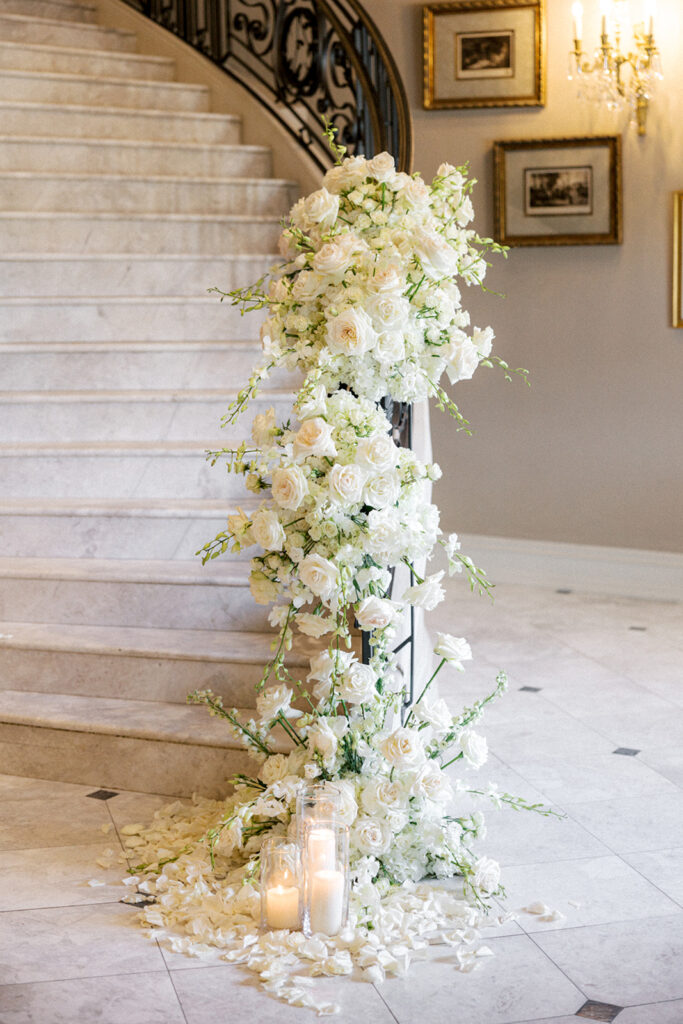 Cascading white floral arrangements cover the wrought iron banister of an elegant marble staircase