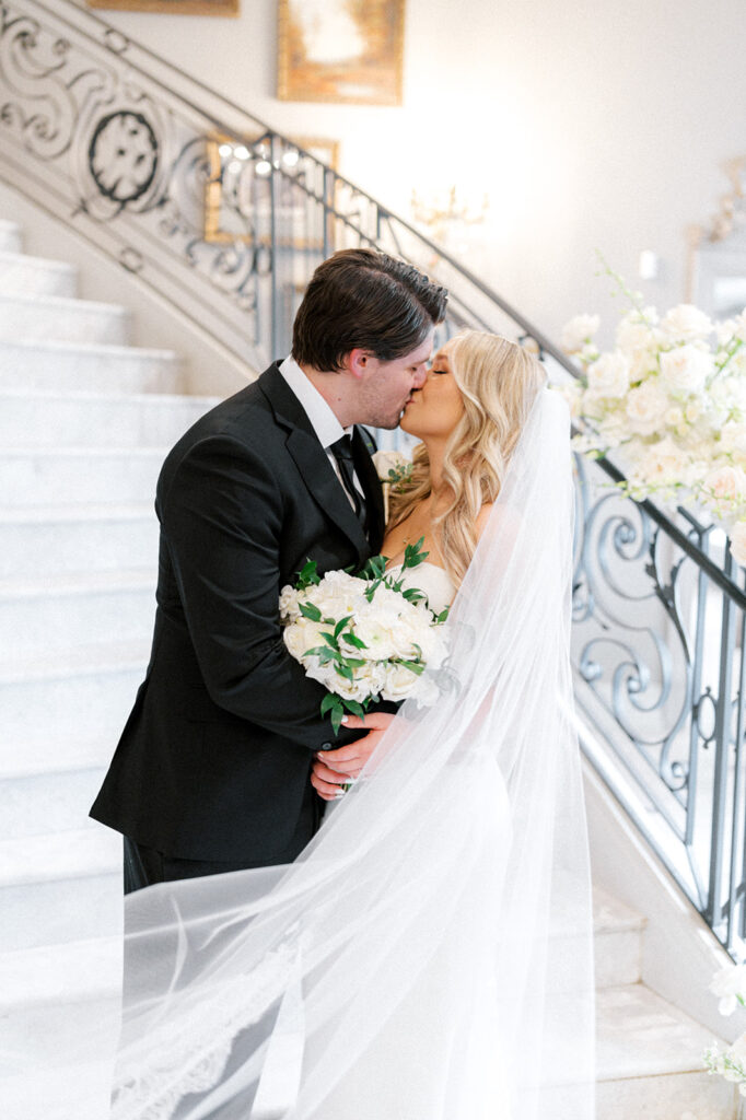 Bride and groom kiss at the foot of an elegant curved marble staircase at the Park Chateau in New Jersey