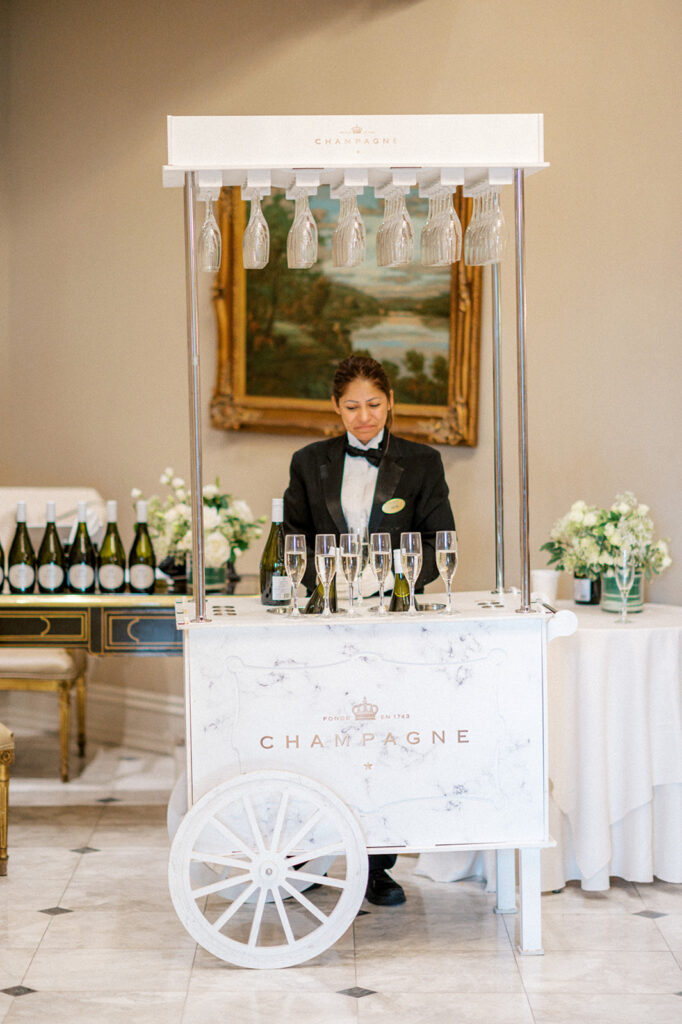 Woman stands behind a small cart holding six champagne flutes 