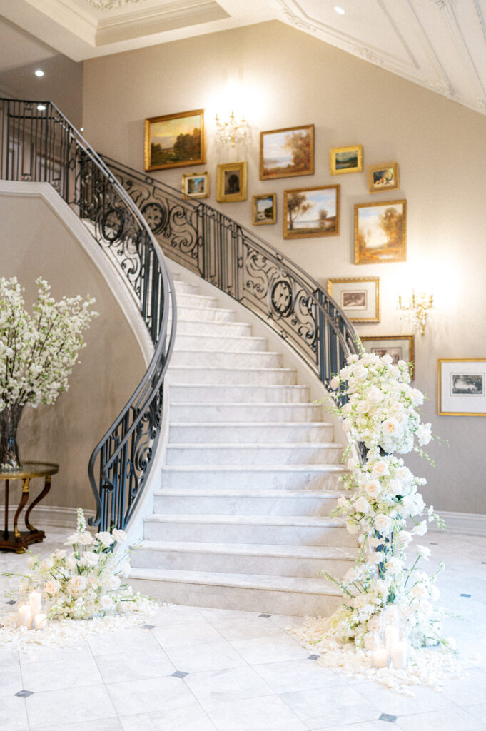 An elegant curved marble staircase is decorated with cascading white floral arrangements and floating candles at the Park Chateau in New Jersey