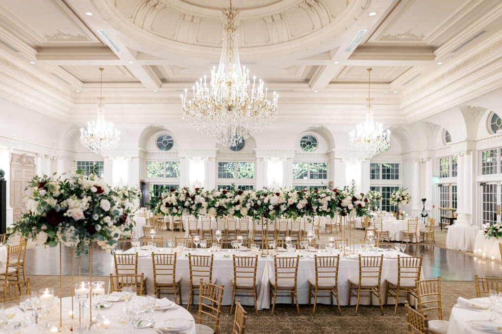 Long banquet table surrounded by gold chiavari chairs is laid for a winter wedding reception in the ballroom at the Park Chateau in New Jersey