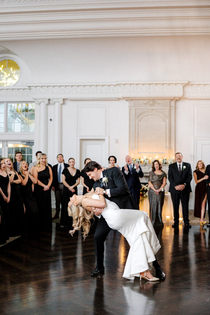 Surrounded by onlookers, groom dips bride back during their first dance in the ballroom at the Park Chateau