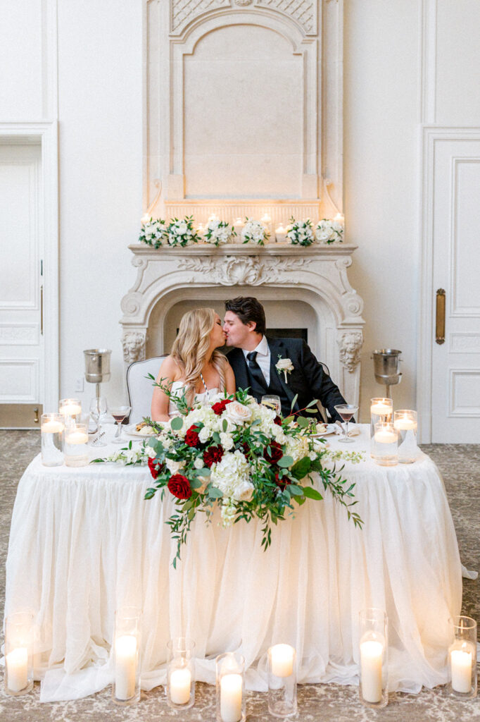 Bride and groom sit at a sweetheart table laid with floating candles and florals in the ballroom at the Park Chateau