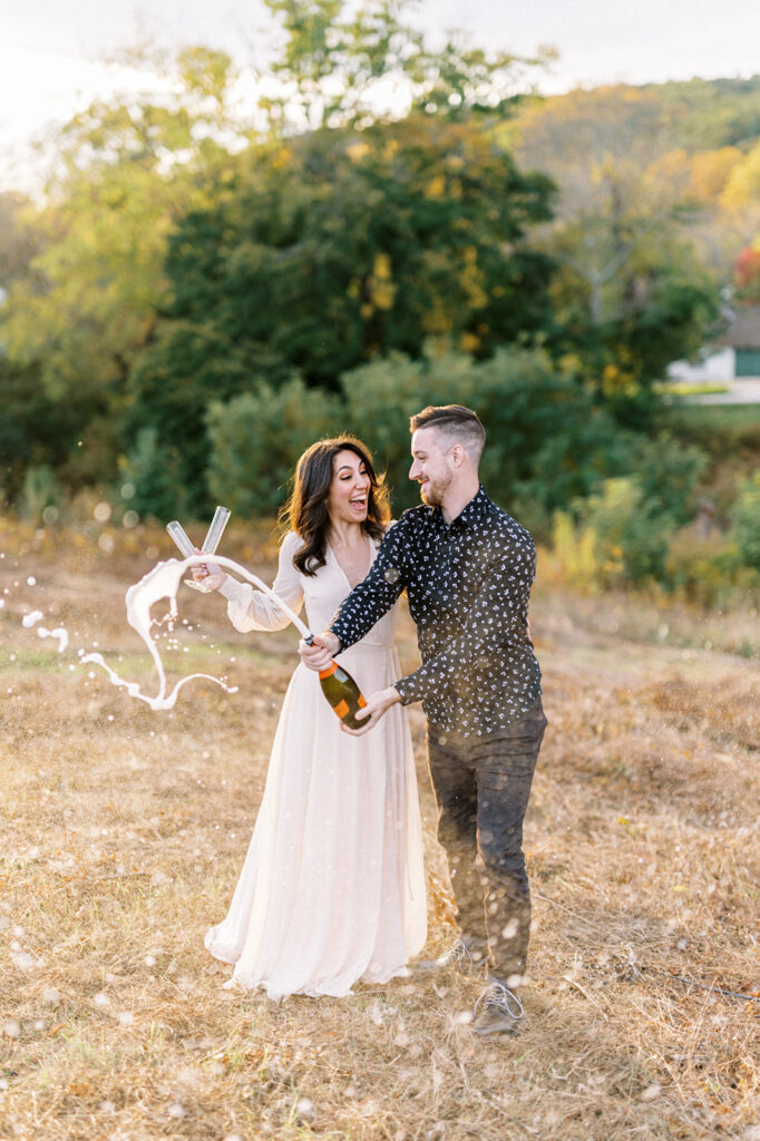 Couple pops a bottle of champagne at Valley Forge | Valley Forge Engagement Photo session by Lindsey Ford Photography