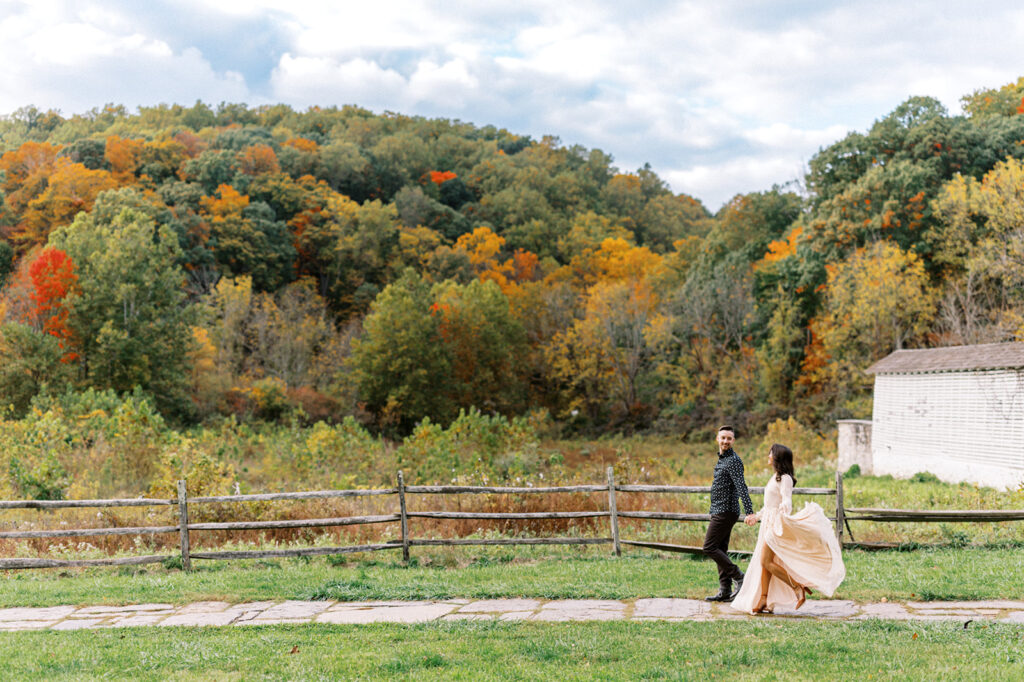 Couple holds hands and walks through Valley Forge looking at PA fall foliage | Valley Forge Engagement Session by Lindsey Ford Photography