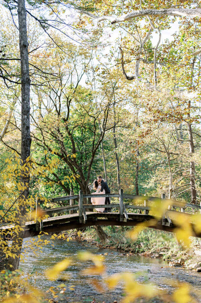 Couple poses on bridge over river in Valley Forge | Valley Forge Engagement Session by Lindsey Ford Photography