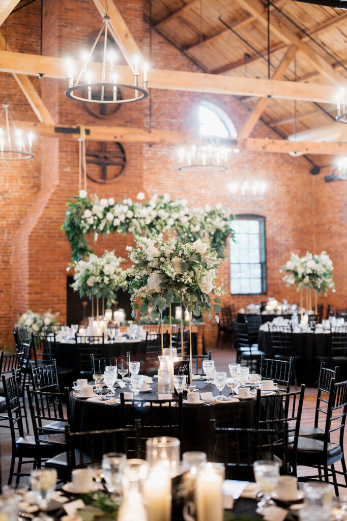 Round tables with black tablecloths black chiavari chairs and white florals with greenery in The Cork Factory Hotel reception space