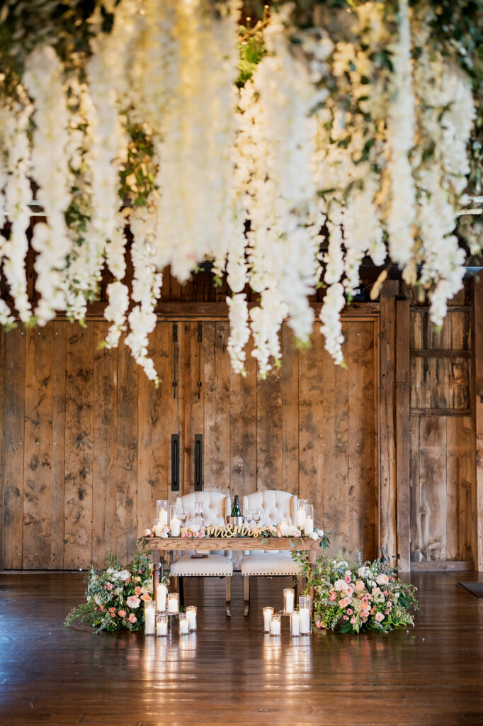Huge floral installation hangs from the ceiling of a wedding reception space over the sweetheart table