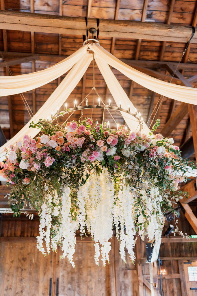 Huge floral installation with white and pink flowers hangs from the ceiling of a wedding reception space