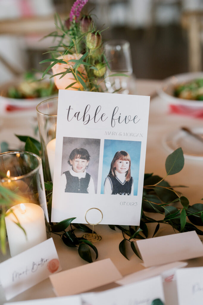 Paper table number marker has the words table five over school photos of two brides as children