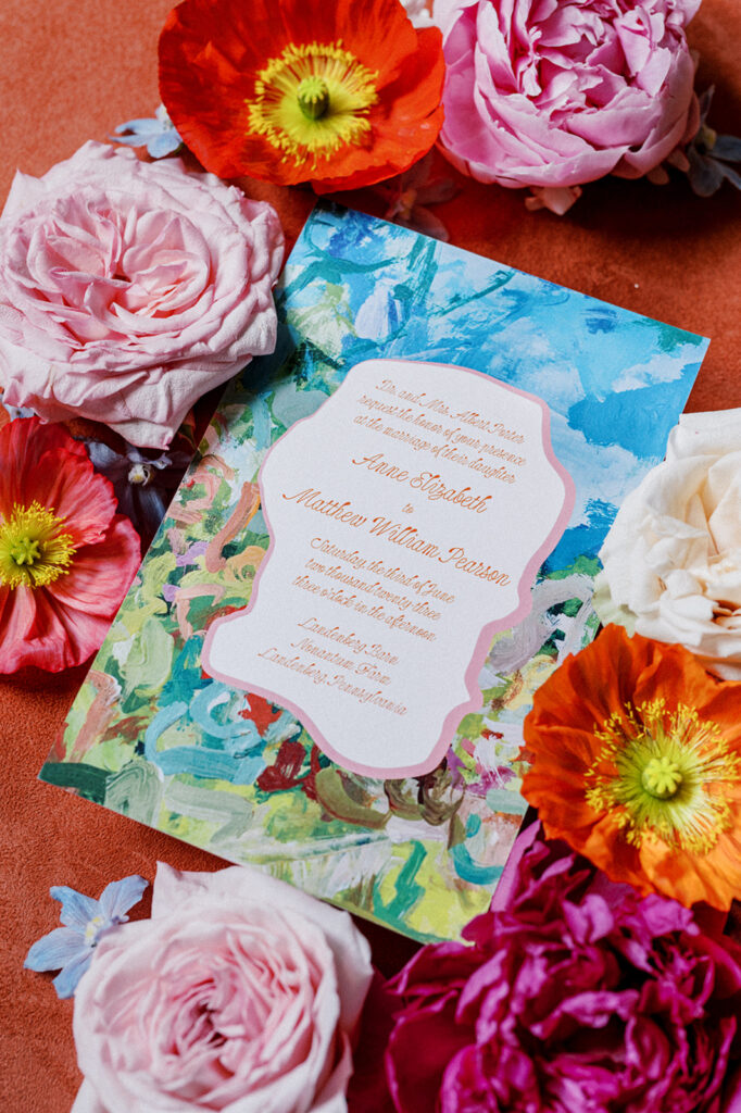Brightly colored wedding detail flat lay with watercolor wedding invitation surrounded by orange and pink florals