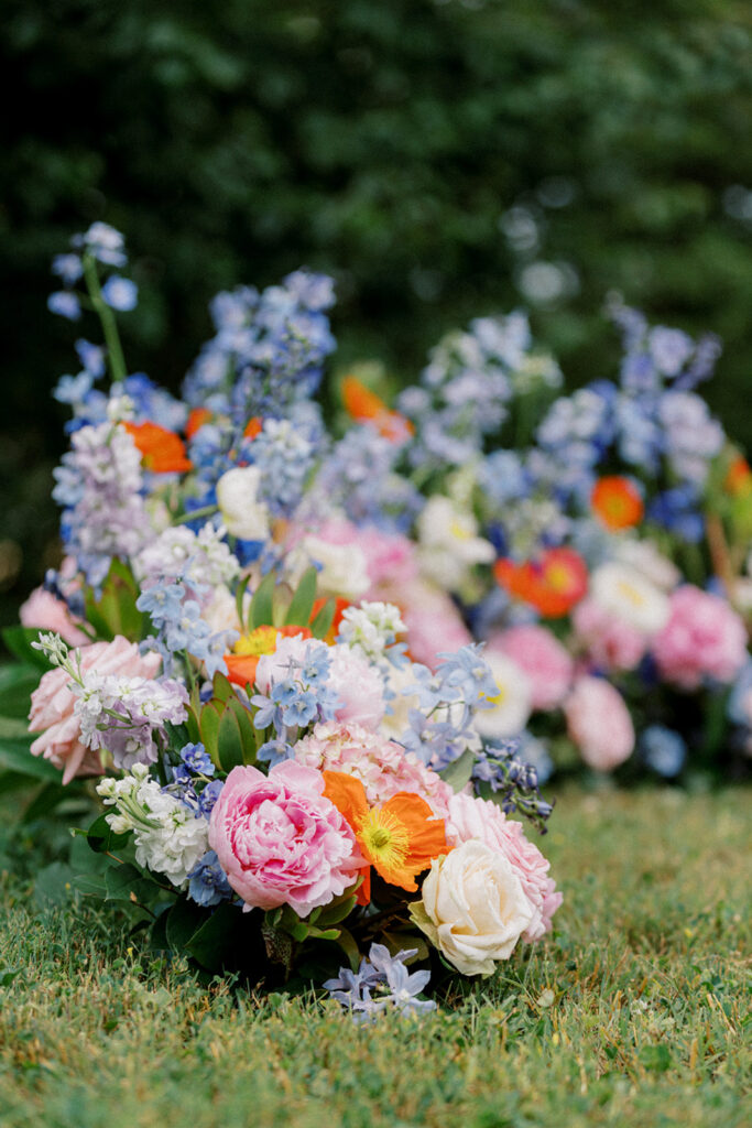 Orange pink white and blue floral installation sits on the ground as a backdrop for a simple wedding ceremony