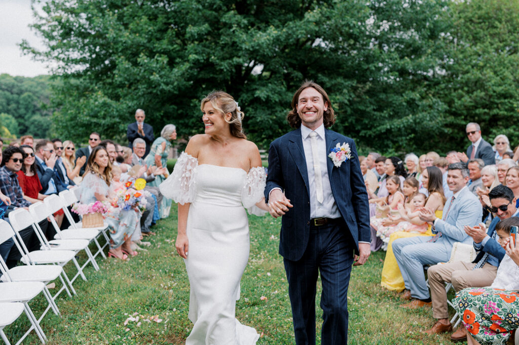 Bride and groom grin as they walk back down the aisle after their wedding ceremony at Landenberg Barn