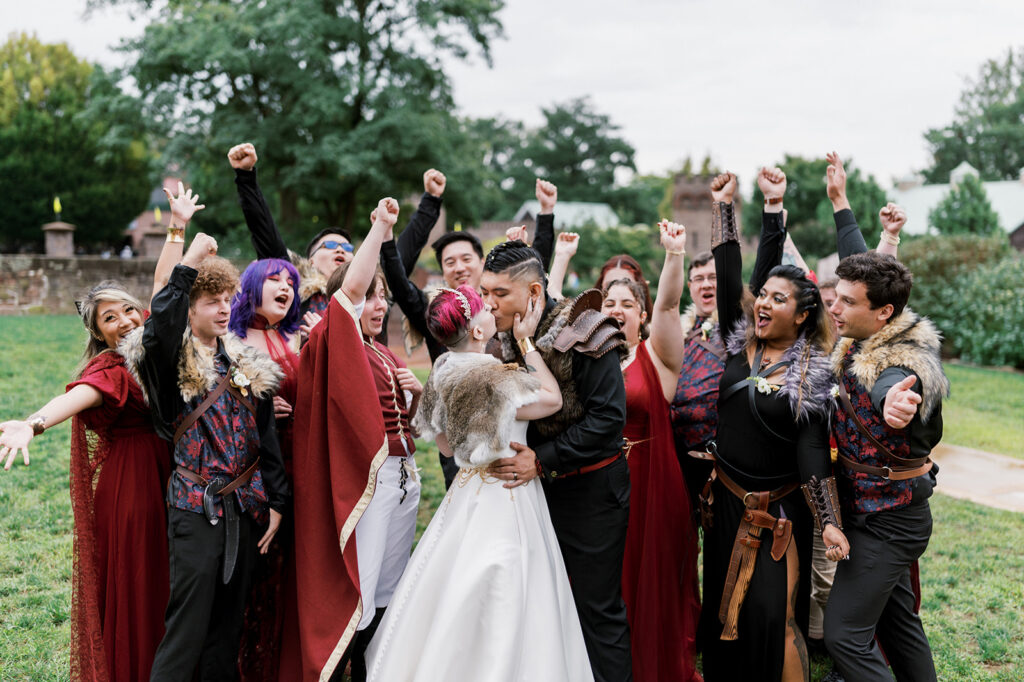 Bridal party wearing Renaissance costumes surround bride and groom and cheer as they kiss at their PA Renaissance Faire fandom wedding
