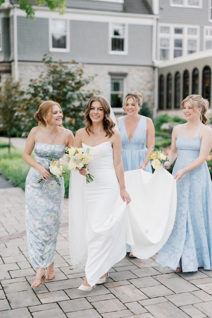 Bride in a white dress and veil walks with her three bridesmaids wearing mix and match pale blue bridesmaid dresses