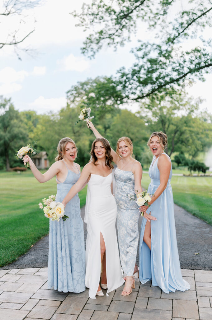 Bride in a white dress and veil poses with her three bridesmaids wearing mix and match pale blue bridesmaid dresses