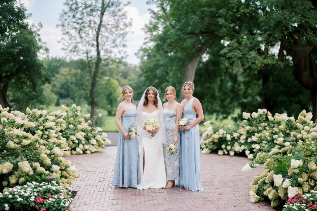 Bride in a white dress and veil stands with her three bridesmaids wearing mix and match pale blue bridesmaid dresses