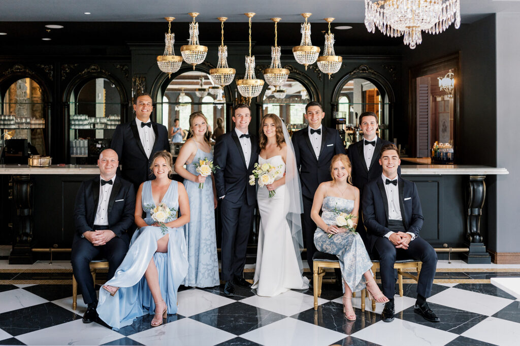 Small bridal party poses under row of gold and crystal chandeliers inside black and white room at The Willows at Ashcombe wedding venue