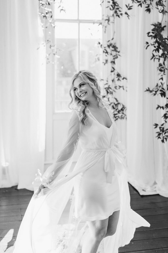 Bride in sheer white robe and half up curled hairstyle looks away and smiles