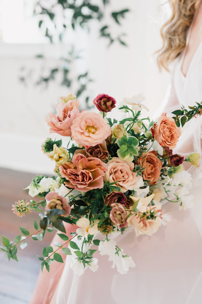 Pink and mauve fall floral bouquet rests on brides knee