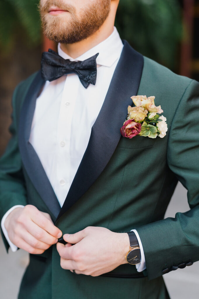 Close up photo of groom in emerald green dinner jacket and black bowtie with a fall floral boutonnière 