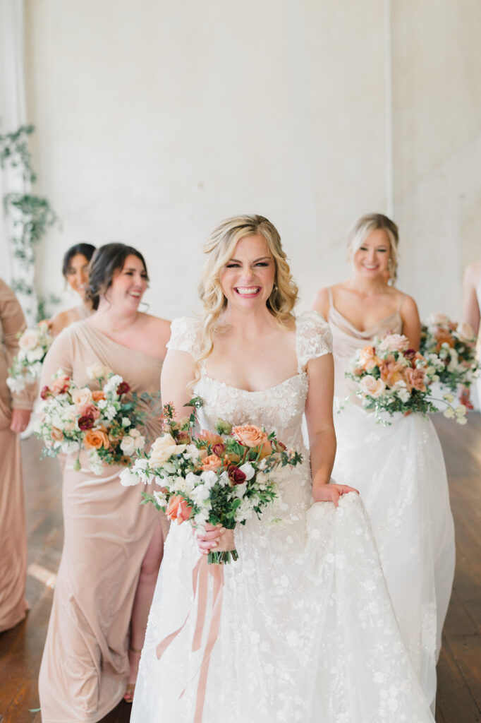 Grinning bride walks with her bridesmaids as her maid of honor holds the train of her dress behind her