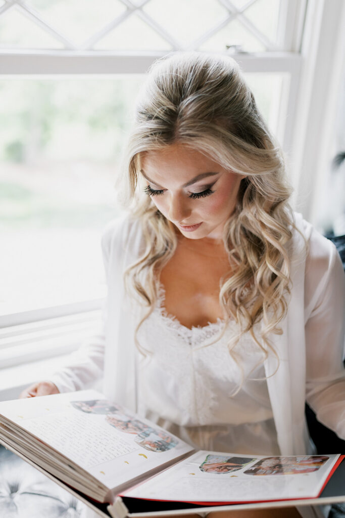 Bride wearing a white robe reads through a handmade album while getting ready for her wedding