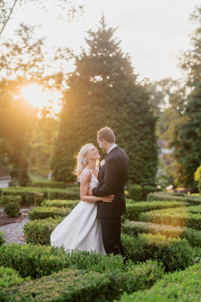 Bride and groom hold each other in the middle of a boxwood hedge garden at Appleford Estate in Villanova, PA at golden hour