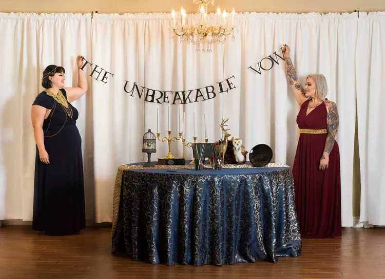 Two women hold up a banner that reads "The unbreakable vow" above a sweetheart table