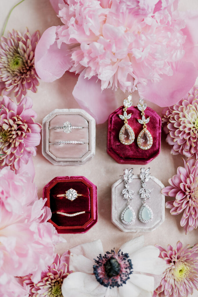 Pink velvet ring boxes surrounded by pink floral cuttings hold gold and silver rings and earrings