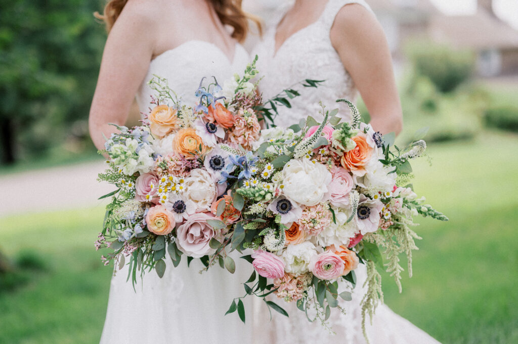 Close up photo of two lush floral bouquets of orange blue and pink during a summer wedding at JJAC