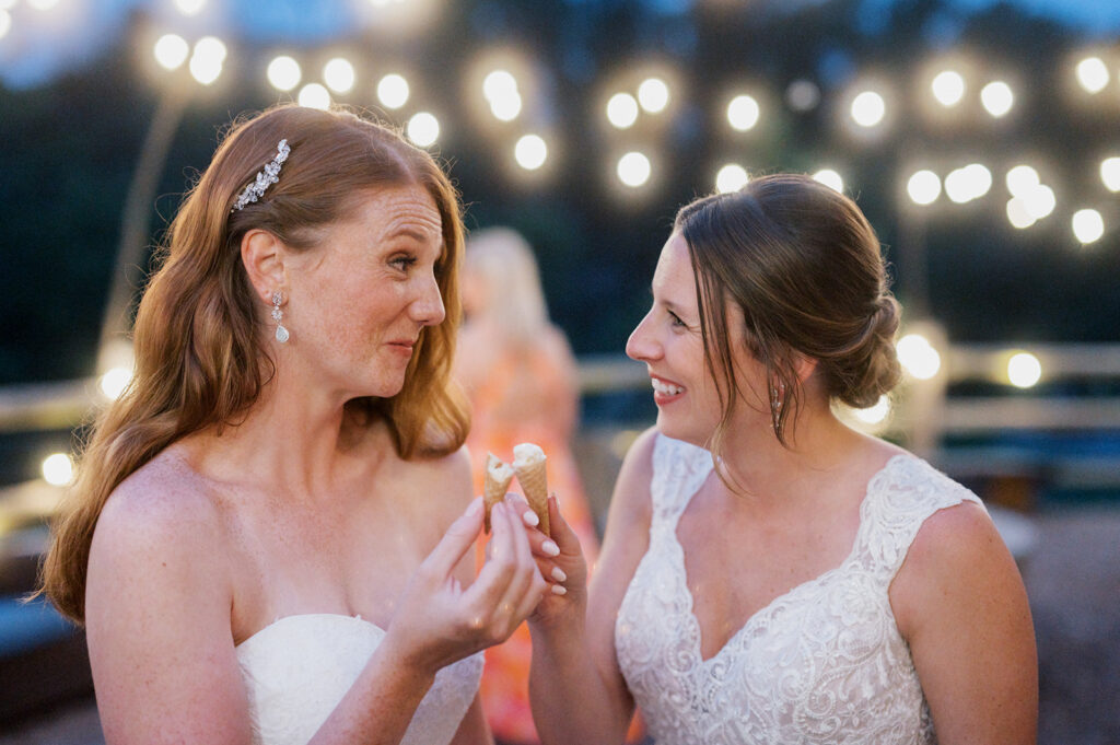 Two brides smile at each other while holding half eaten ice cream cones during their wedding reception