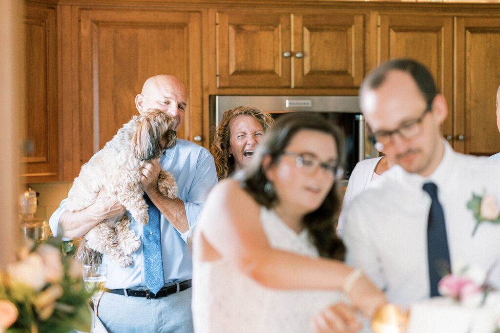 Father and mother of the bride watch as bride and groom cut wedding cake in family kitchen