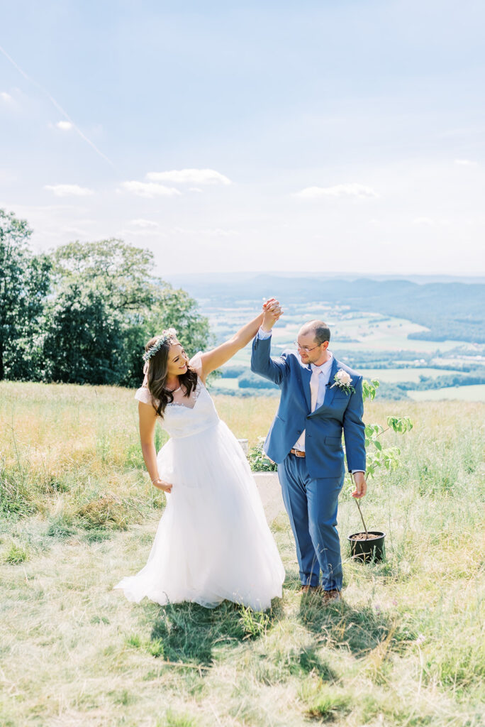 Bride and groom hold hands and look at each other as they stand on a hillside overlooking a grassy valley below