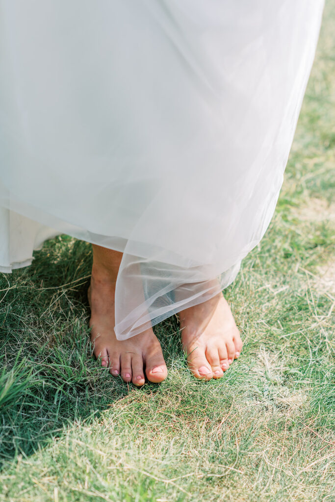 Close up photo of brides bare feet standing in a field of grass