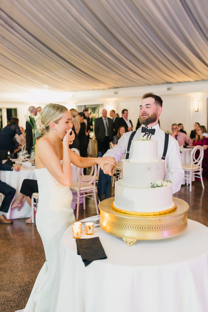 Bride and groom taste three tier white wedding cake at their Lake House Inn wedding reception 