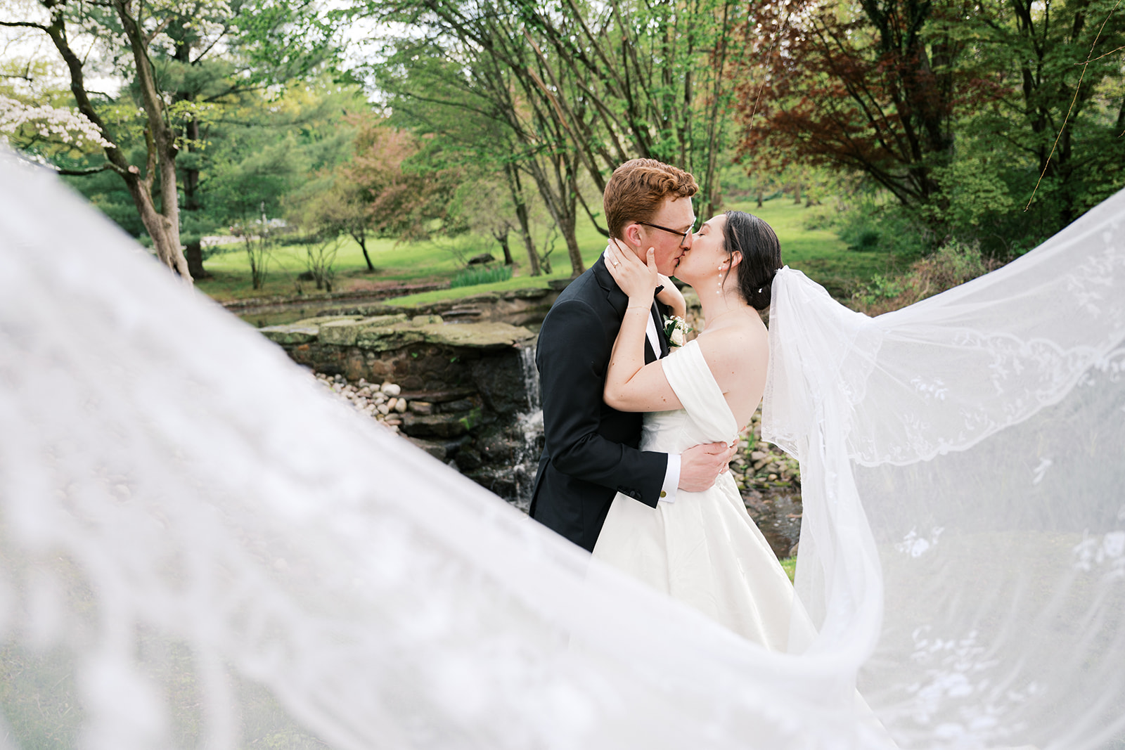 Bride and groom kiss in a garden behind a veil blowing in the wind | Lindsey Ford Photography at Appleford Estate