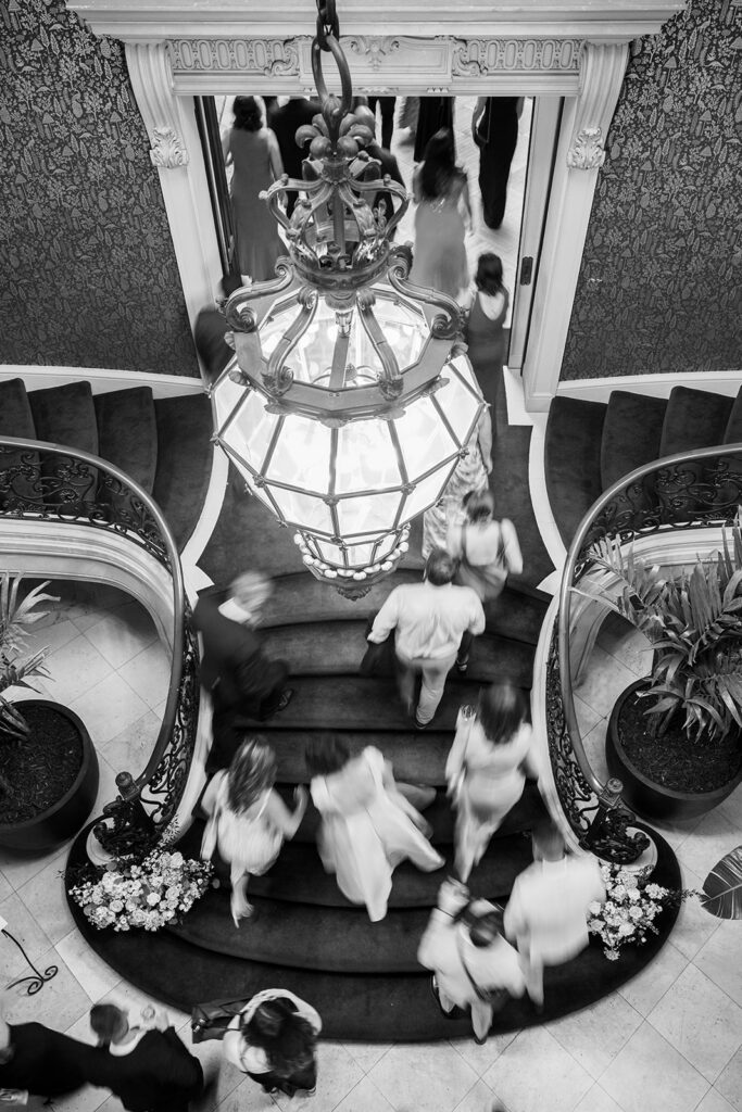 Motion blur overhead view of wedding guests walking up a grand staircase under a statement light fixture at Elkins Estate wedding event venue