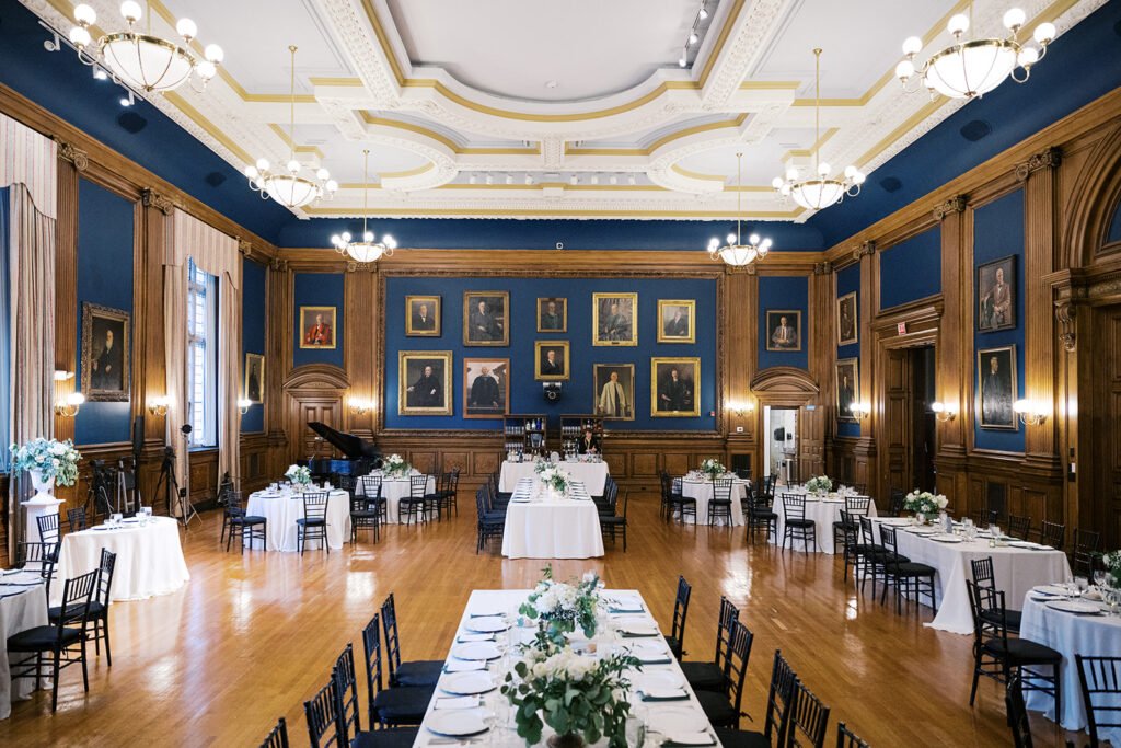 Blue and wood-paneled room, with portraits lining the walls and natural light streaming through tall windows
