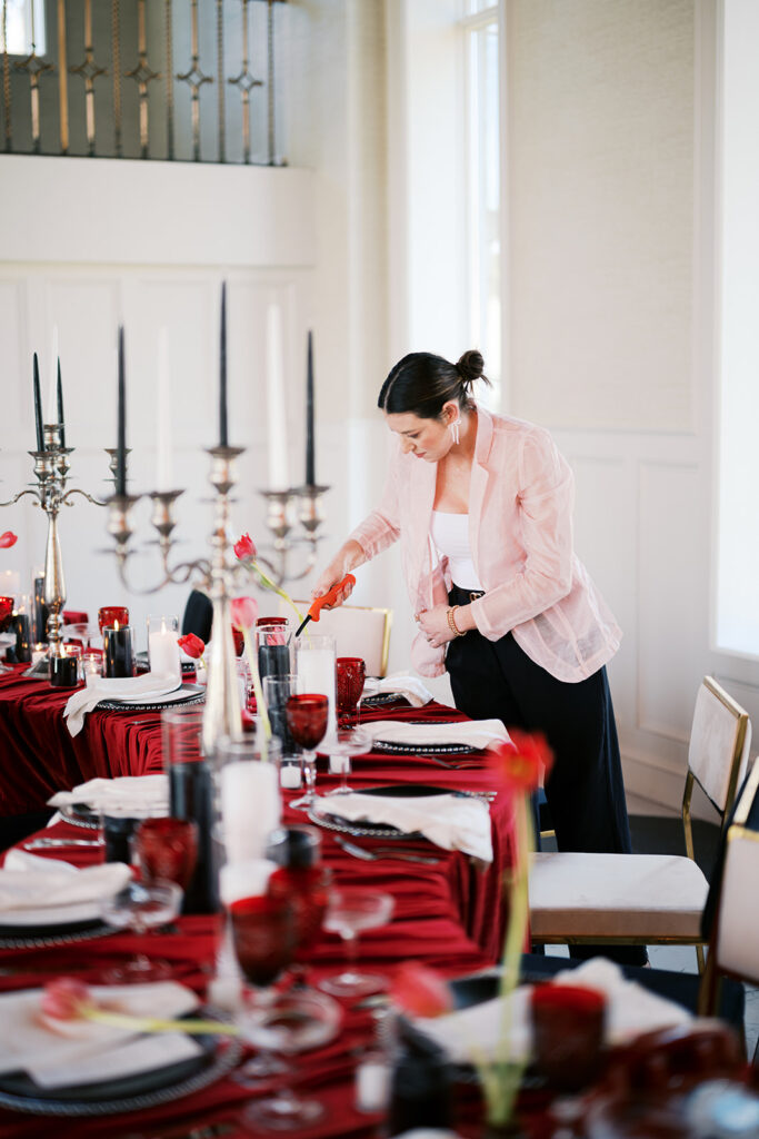 Wedding planner lights candles on a banquet table covered in red linen and black and white wedding reception decor at Elkins Estate | Lindsey Ford Photography