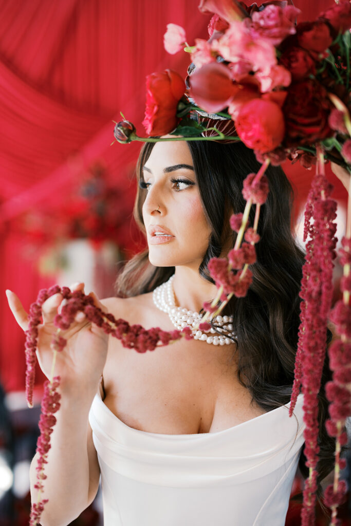 Bride poses with all red bouquet over her head against wedding ceremony backdrop of dark red draping at Elkins Estate in PA