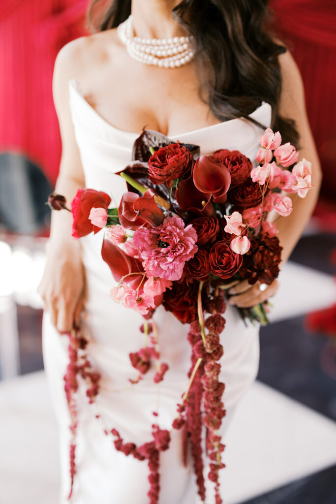 Close up of bride holding all red bouquet against wedding ceremony backdrop of dark red draping at Elkins Estate in PA