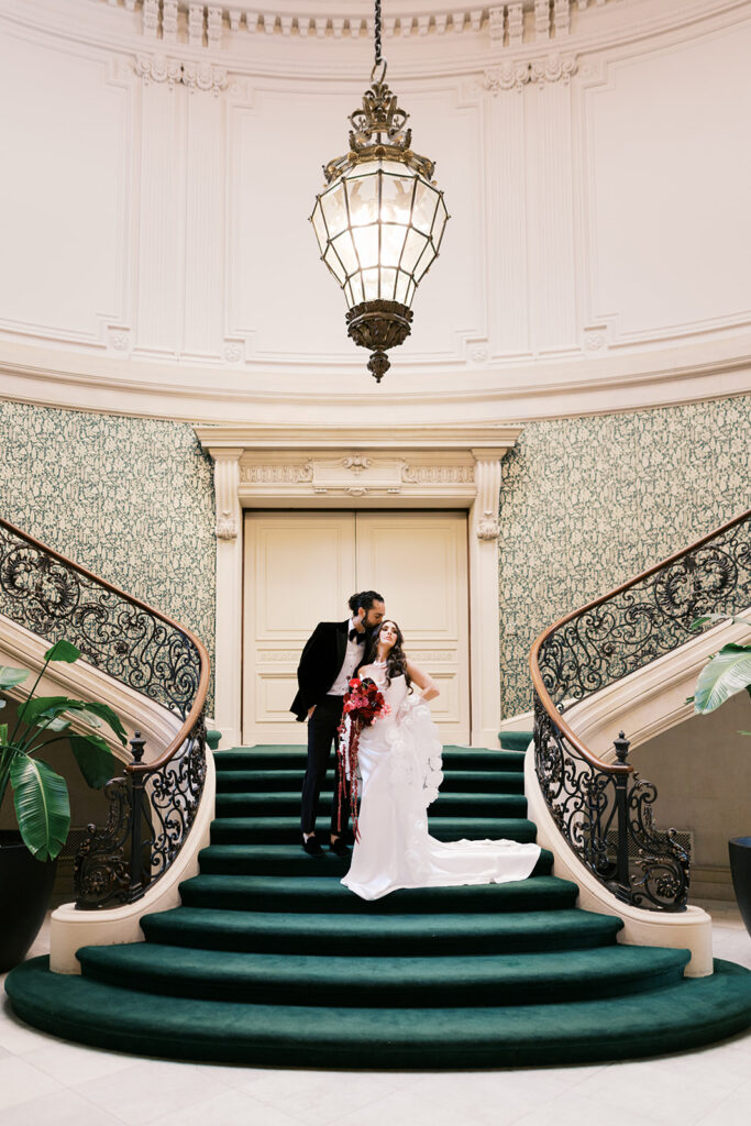 Bride and groom pose on a velvet green staircase with wrought iron banister at Elkins Estate in PA