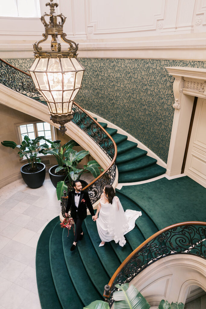 Bride and groom walk down a velvet green staircase with wrought iron banister at Elkins Estate in PA
