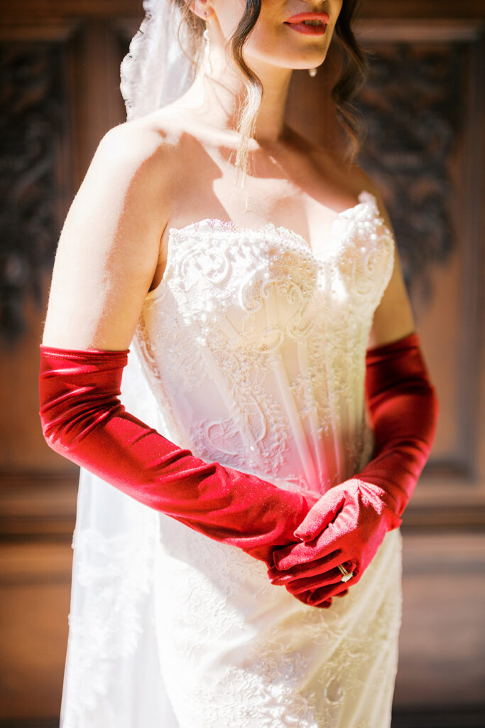 Close up of bride wearing beaded corset top dress and elbow length red gloves