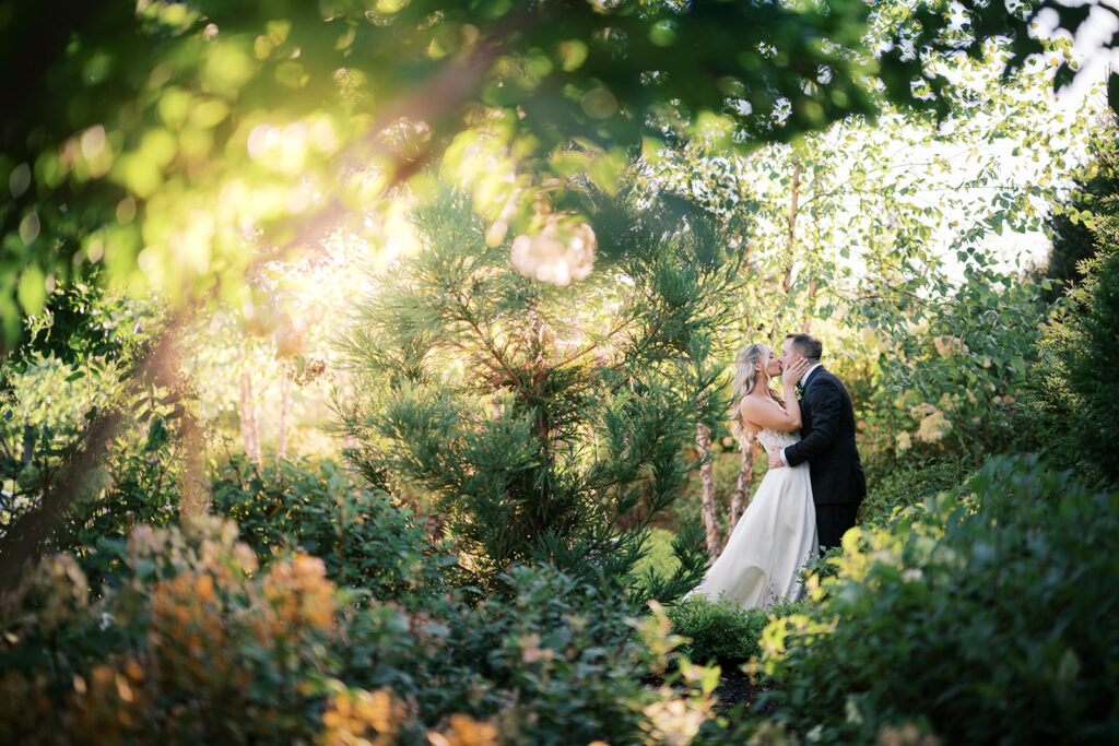 Bride and groom stand and kiss in the middle of the woods with sun rays beaming through the leaves | Lindsey Ford Photography at The Gardens at Applecross