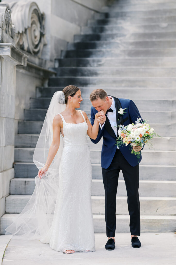 Groom kisses brides hand in front of stone staircase at the Merchants Exchange building in the Old Philly sector of Philadelphia | Lindsey  Ford Photography