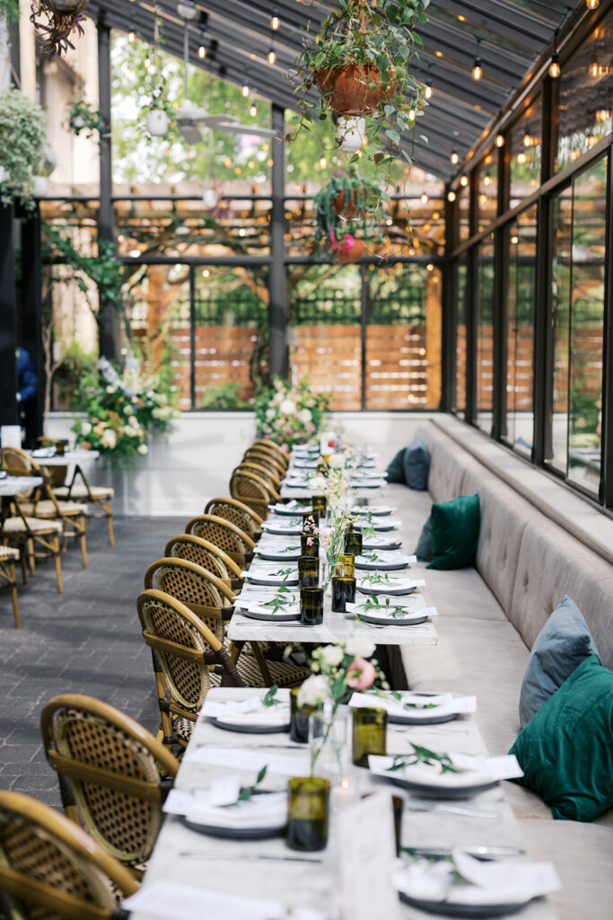 Row of wedding reception tables are set with plates and aligned against a wall of booth seating on one side and set with cafe chairs on the other side at Osteria in Philly